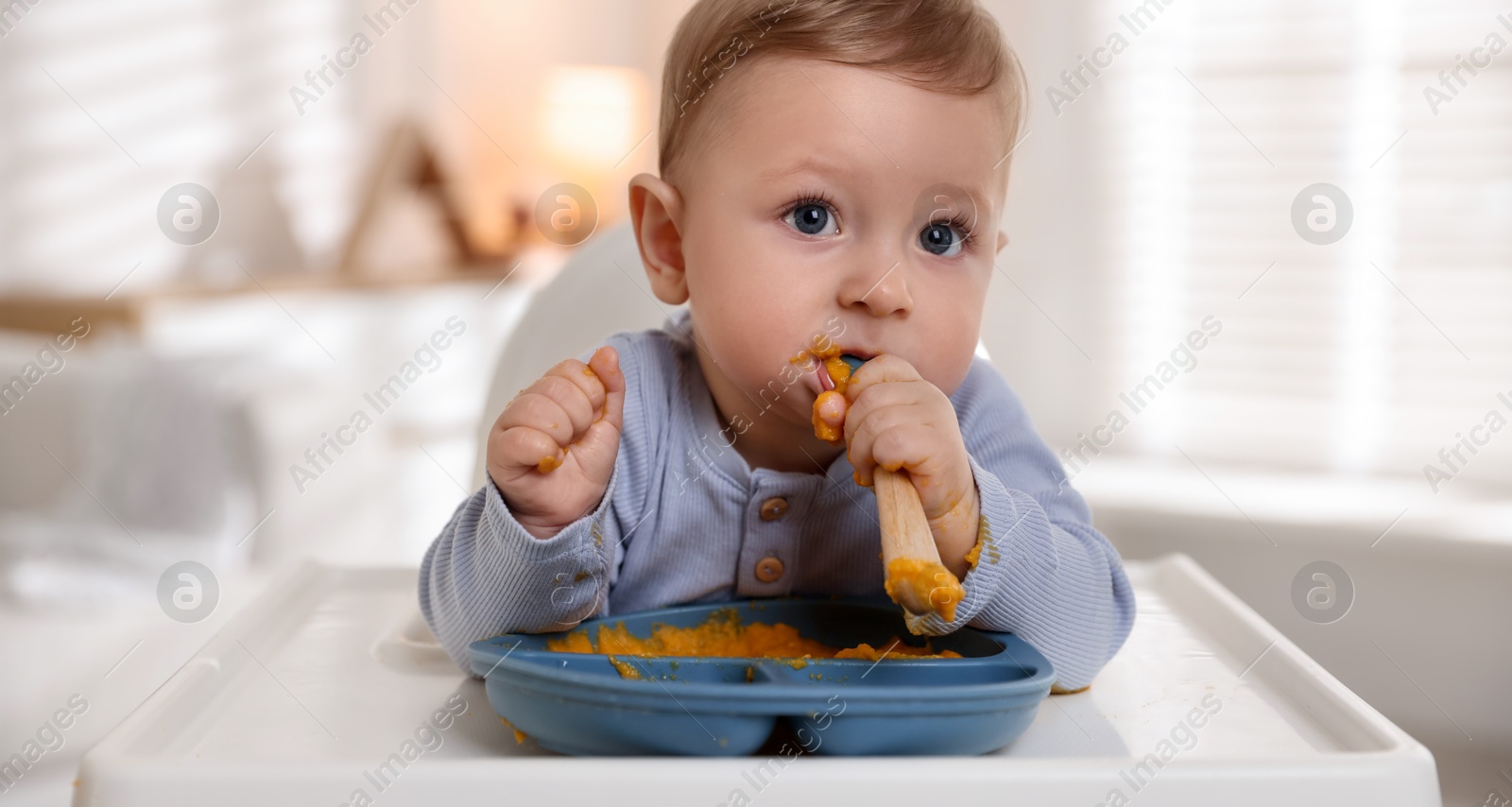 Photo of Cute little baby eating healthy food in high chair indoors