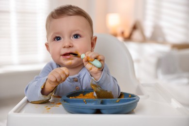 Photo of Cute little baby eating healthy food in high chair indoors