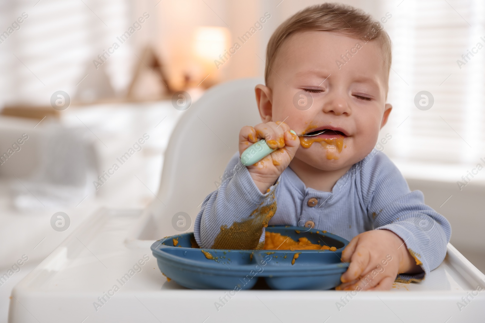 Photo of Cute little baby eating healthy food in high chair indoors