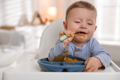 Cute little baby eating healthy food in high chair indoors