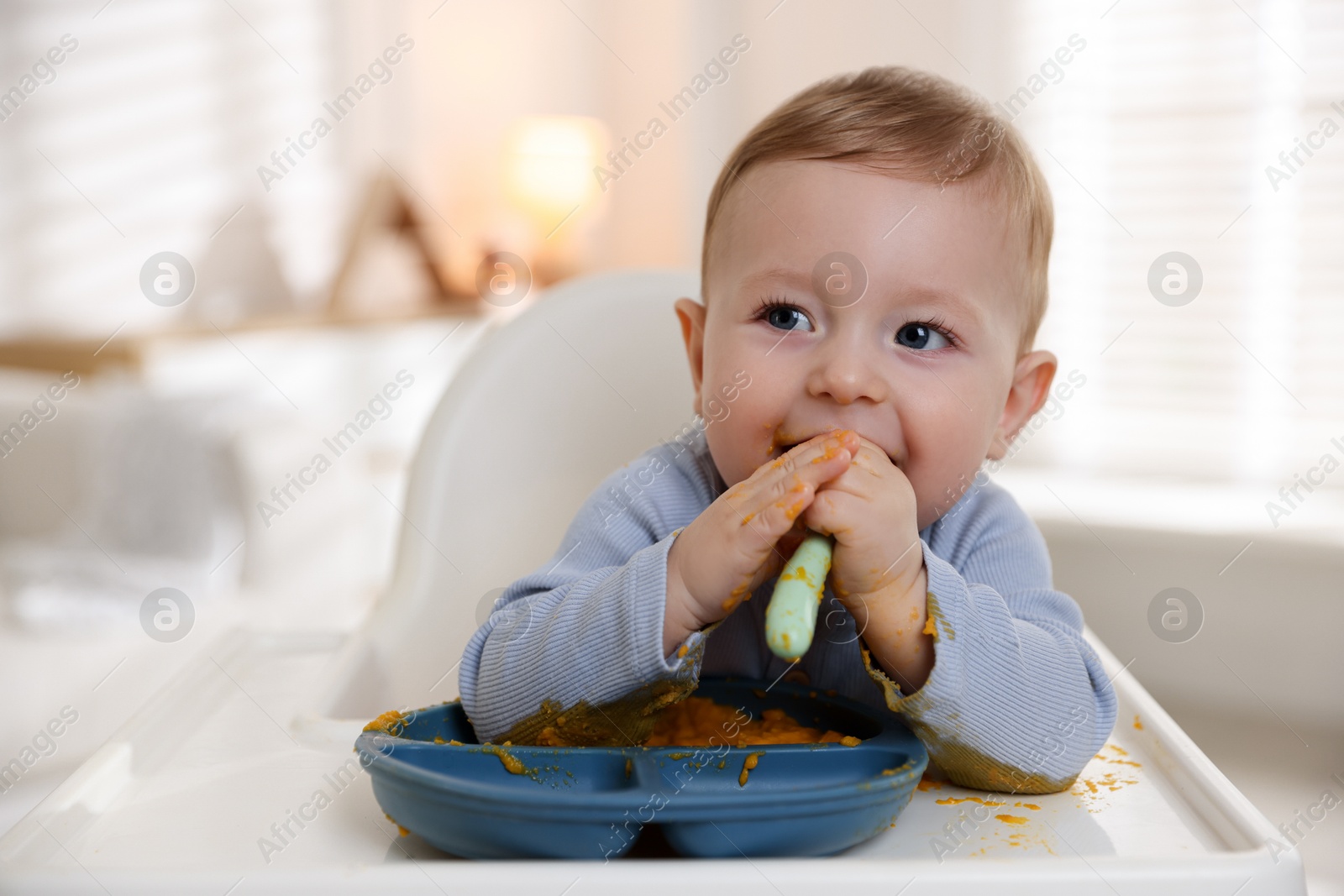 Photo of Cute little baby eating healthy food in high chair indoors