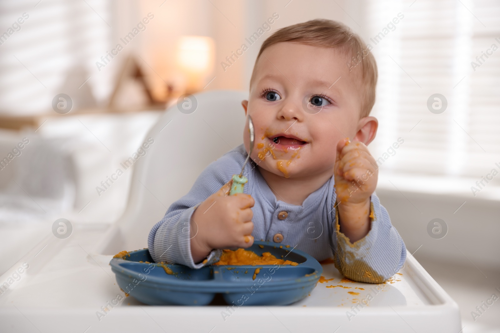 Photo of Cute little baby eating healthy food in high chair indoors