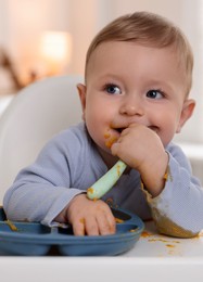 Photo of Cute little baby eating healthy food in high chair indoors