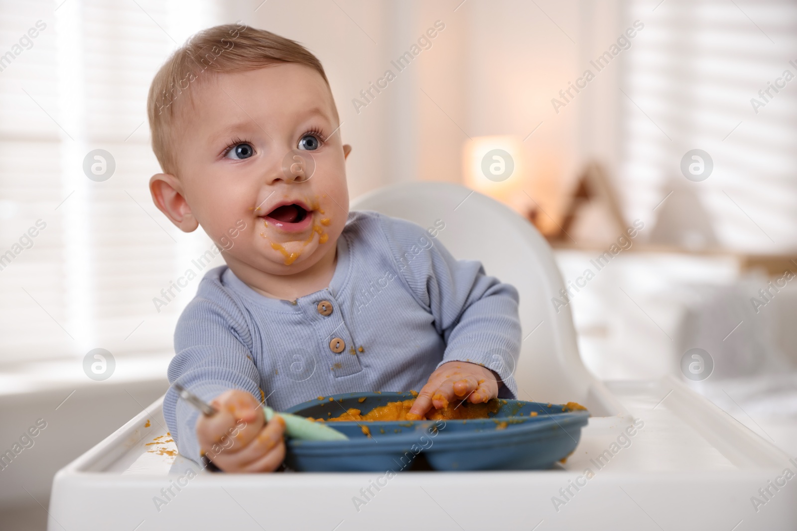 Photo of Cute little baby eating healthy food in high chair indoors