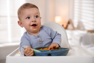 Cute little baby eating healthy food in high chair indoors