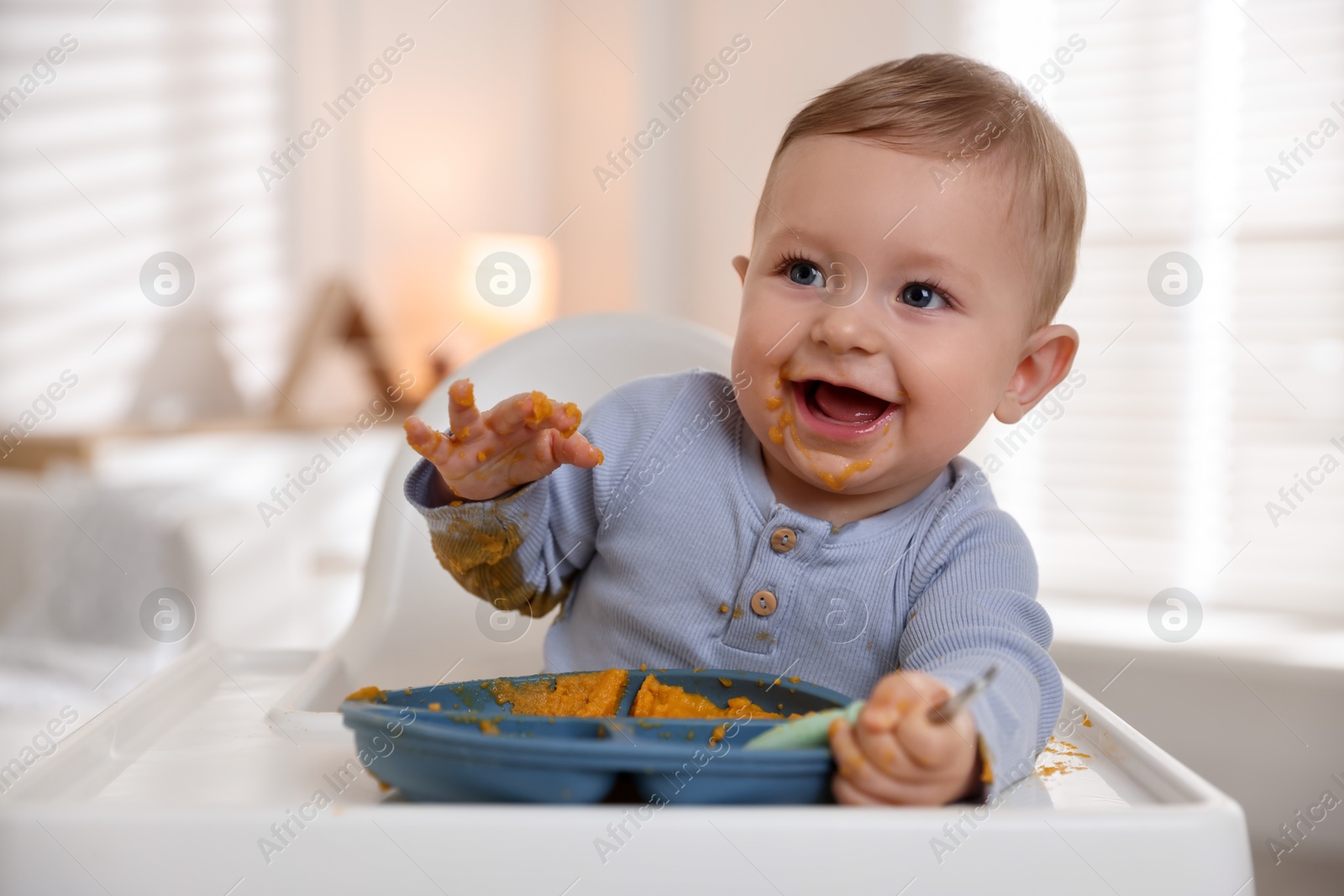 Photo of Cute little baby eating healthy food in high chair indoors