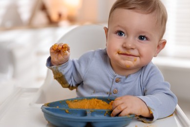 Cute little baby eating healthy food in high chair indoors