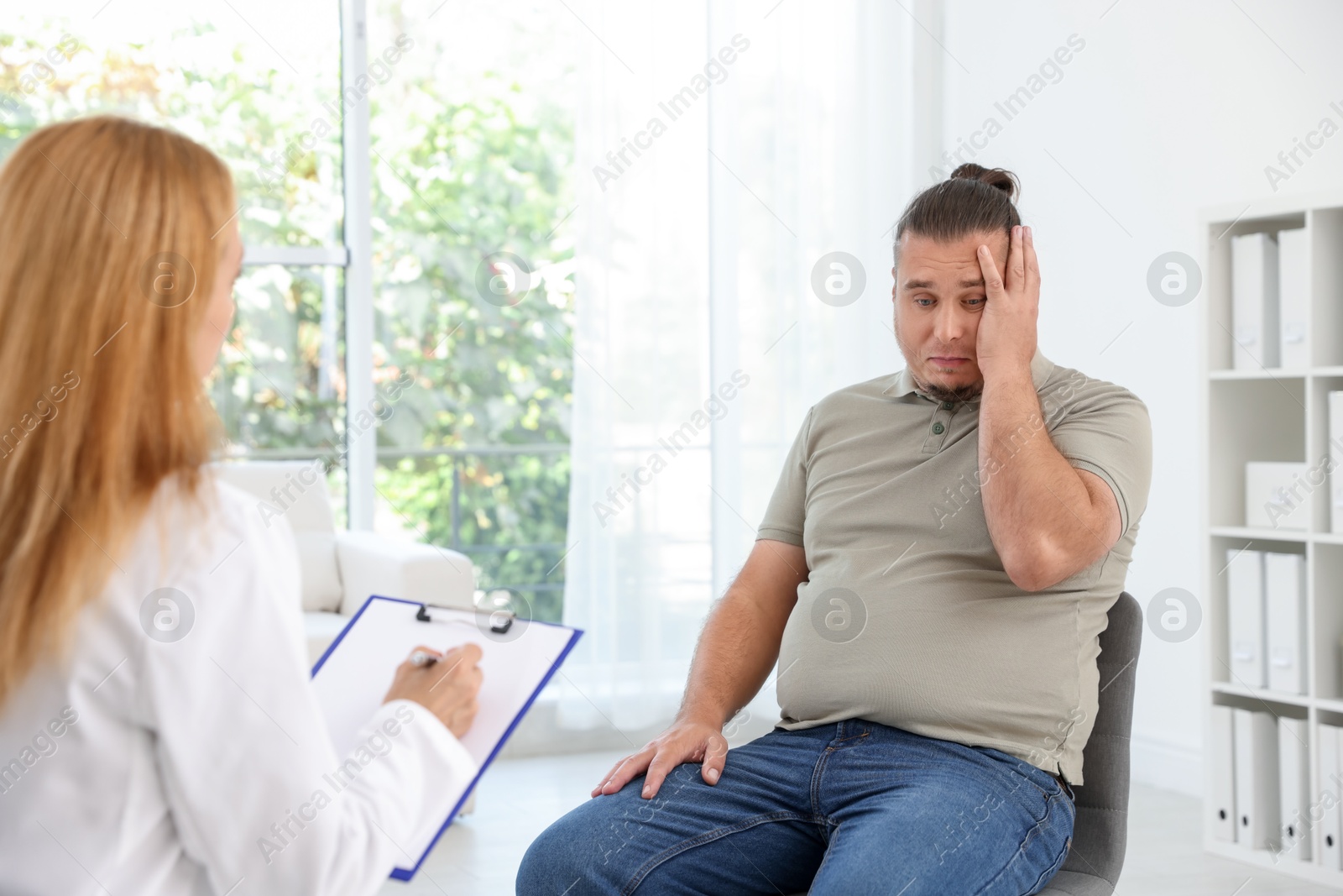 Photo of Nutritionist with clipboard consulting overweight man in clinic