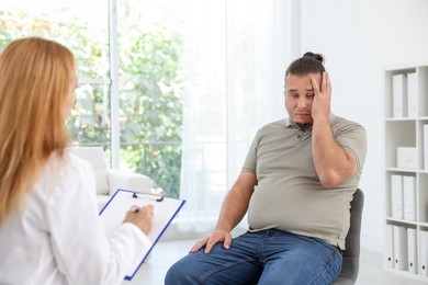 Nutritionist with clipboard consulting overweight man in clinic