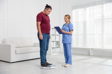 Photo of Overweight man standing on scales during consultation with nutritionist in clinic