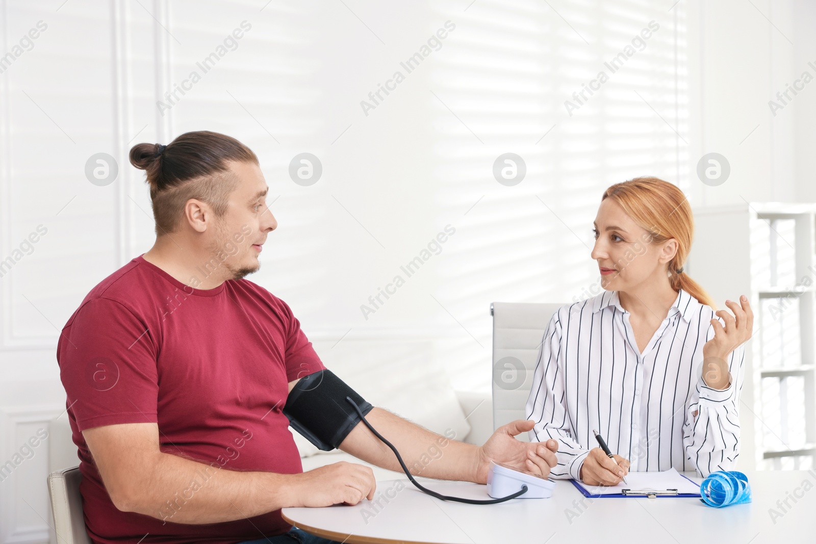 Photo of Nutritionist measuring overweight patient's blood pressure at table in clinic