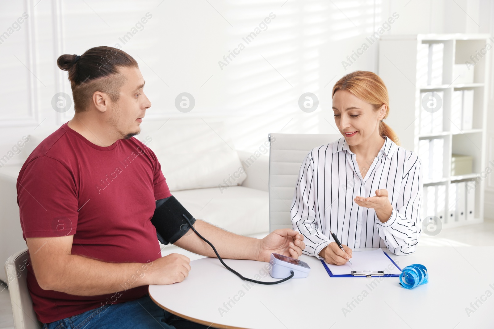 Photo of Nutritionist measuring overweight patient's blood pressure at table in clinic