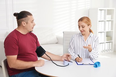 Photo of Nutritionist measuring overweight patient's blood pressure at table in clinic