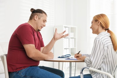 Photo of Overweight man having consultation with nutritionist at table in clinic