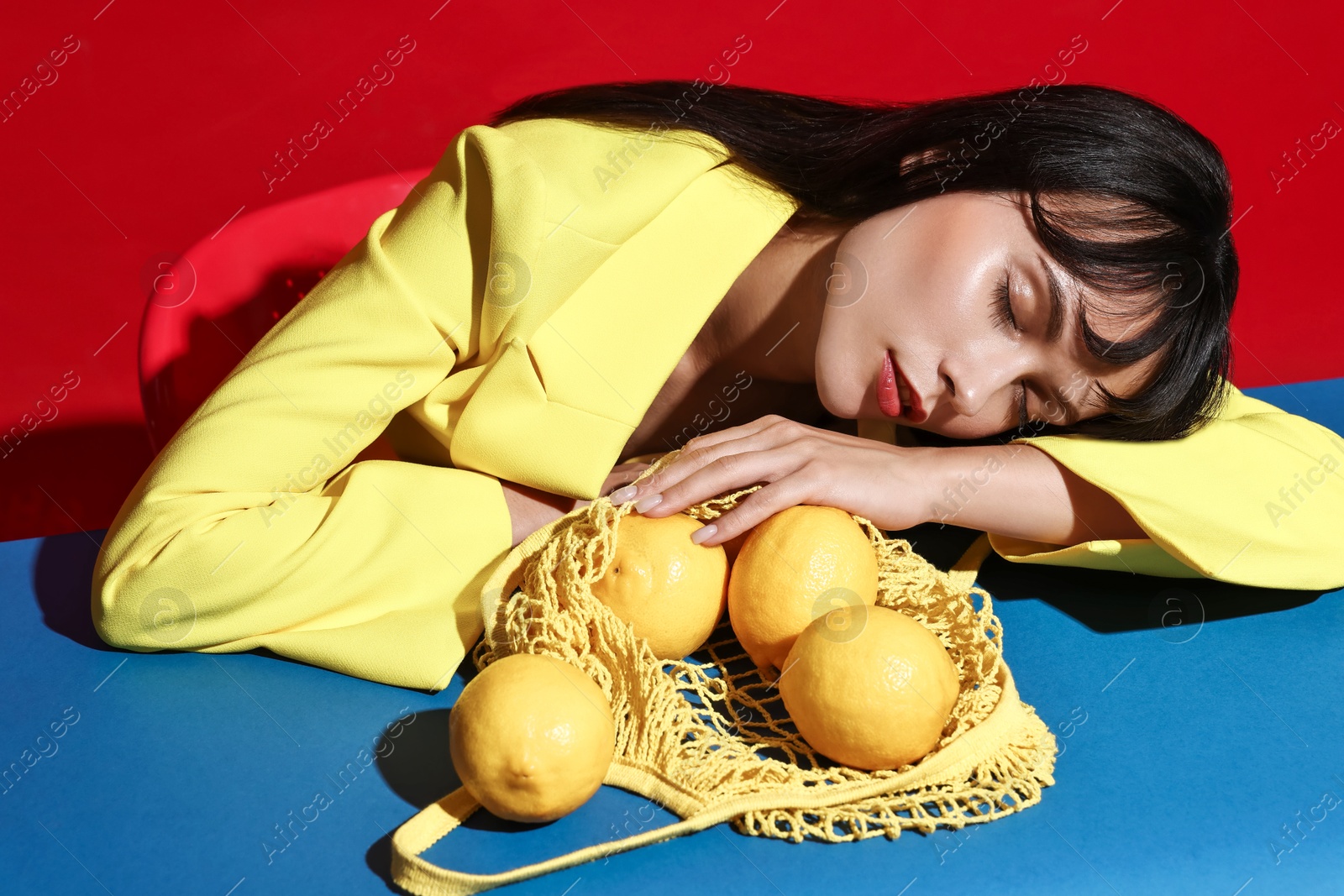 Photo of Woman with net bag and lemons at blue table on red background