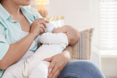 Photo of Mother feeding her cute baby indoors, closeup