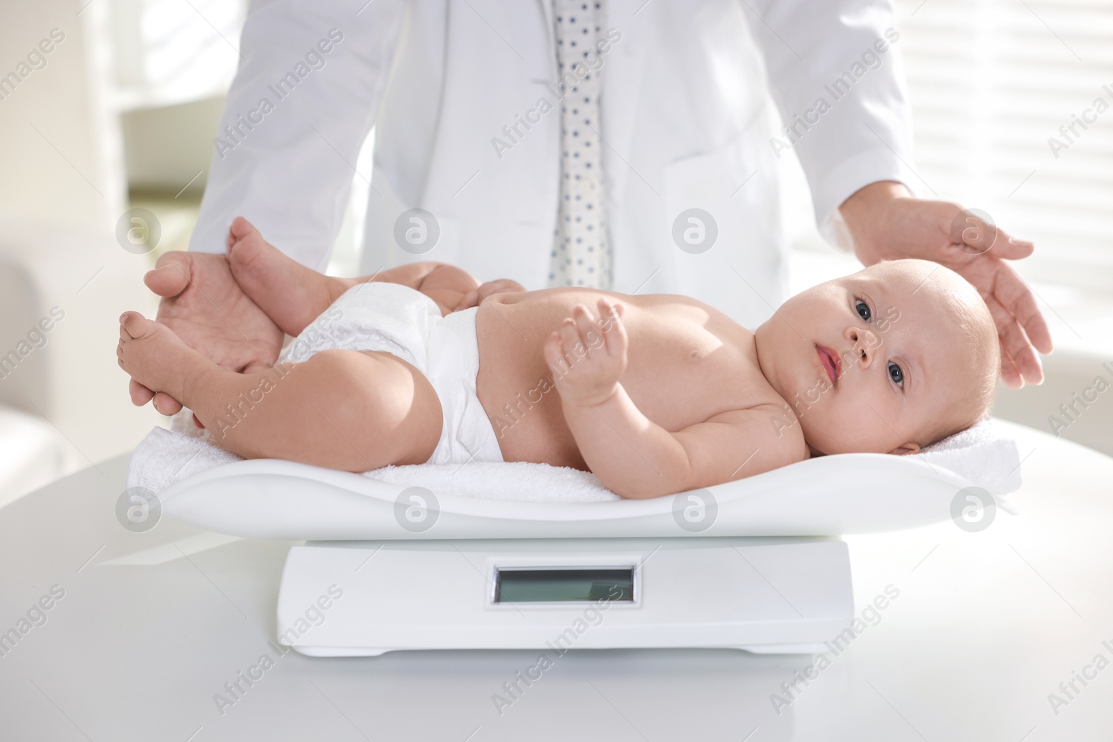 Photo of Pediatrician weighting little child in clinic, closeup. Checking baby's health