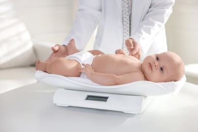 Photo of Pediatrician weighting little child in clinic, closeup. Checking baby's health