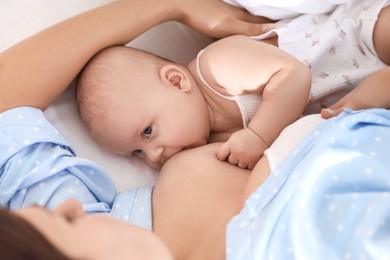 Photo of Mother breastfeeding her little baby on bed at home, closeup