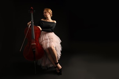 Photo of Beautiful young woman with cello on black background, space for text