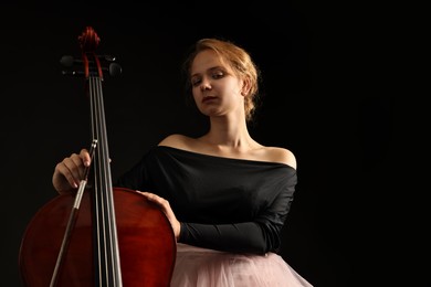 Beautiful young woman with cello on black background