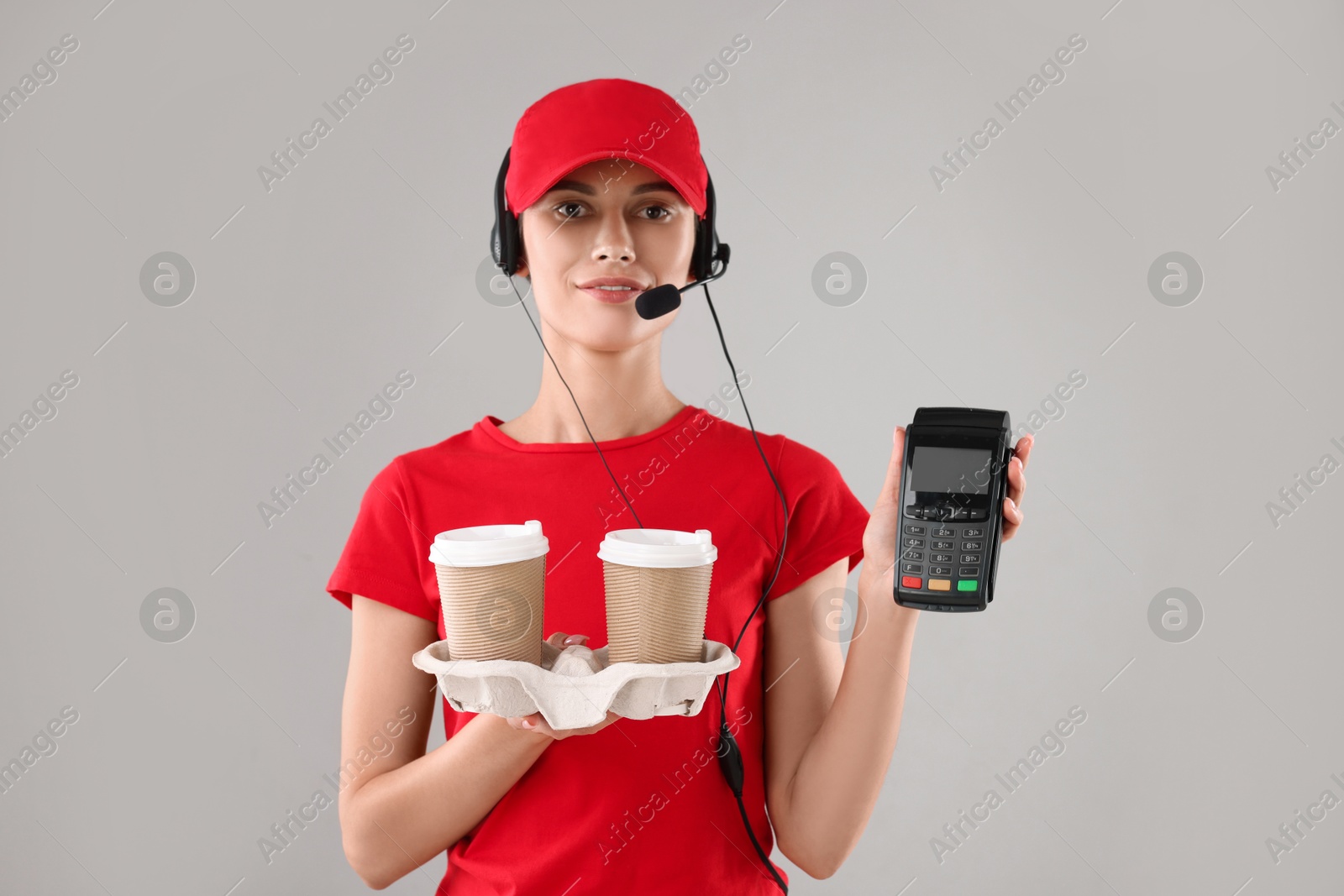 Photo of Fast-food worker with paper cups and payment terminal on gray background