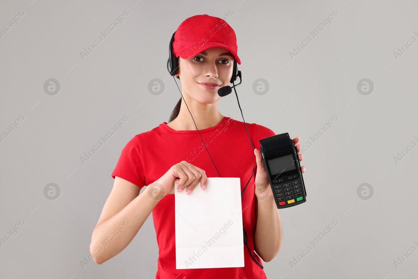 Photo of Fast-food worker with paper bag and payment terminal on gray background