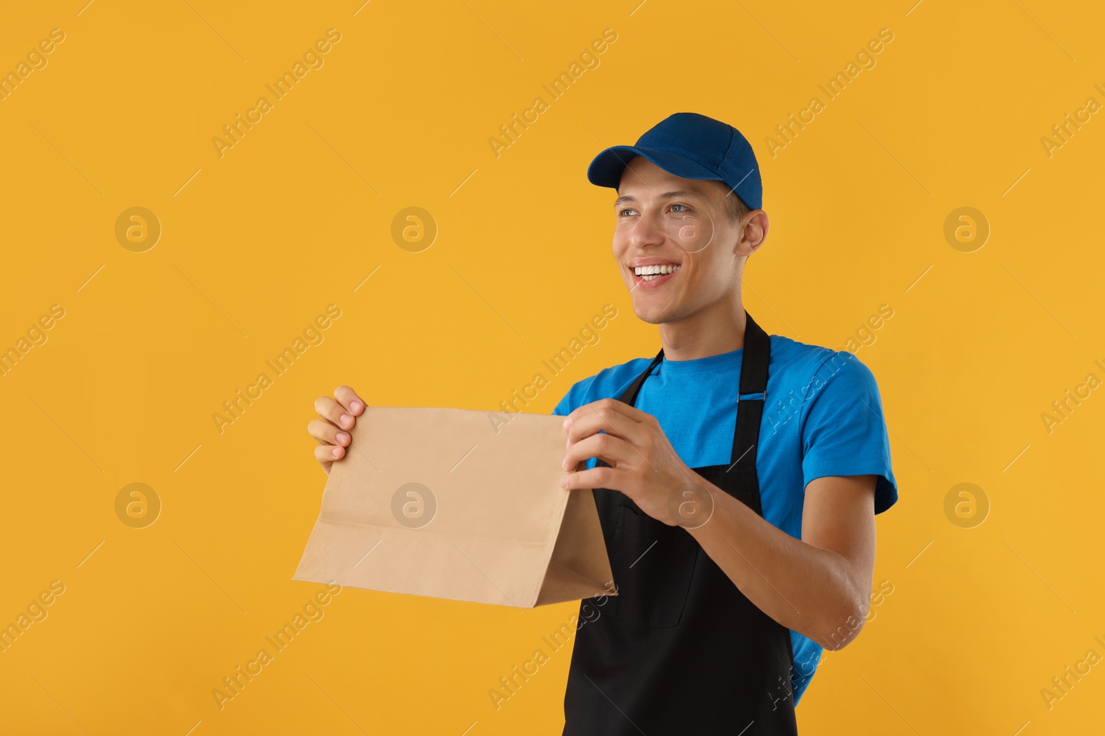 Photo of Fast-food worker with paper bag on orange background