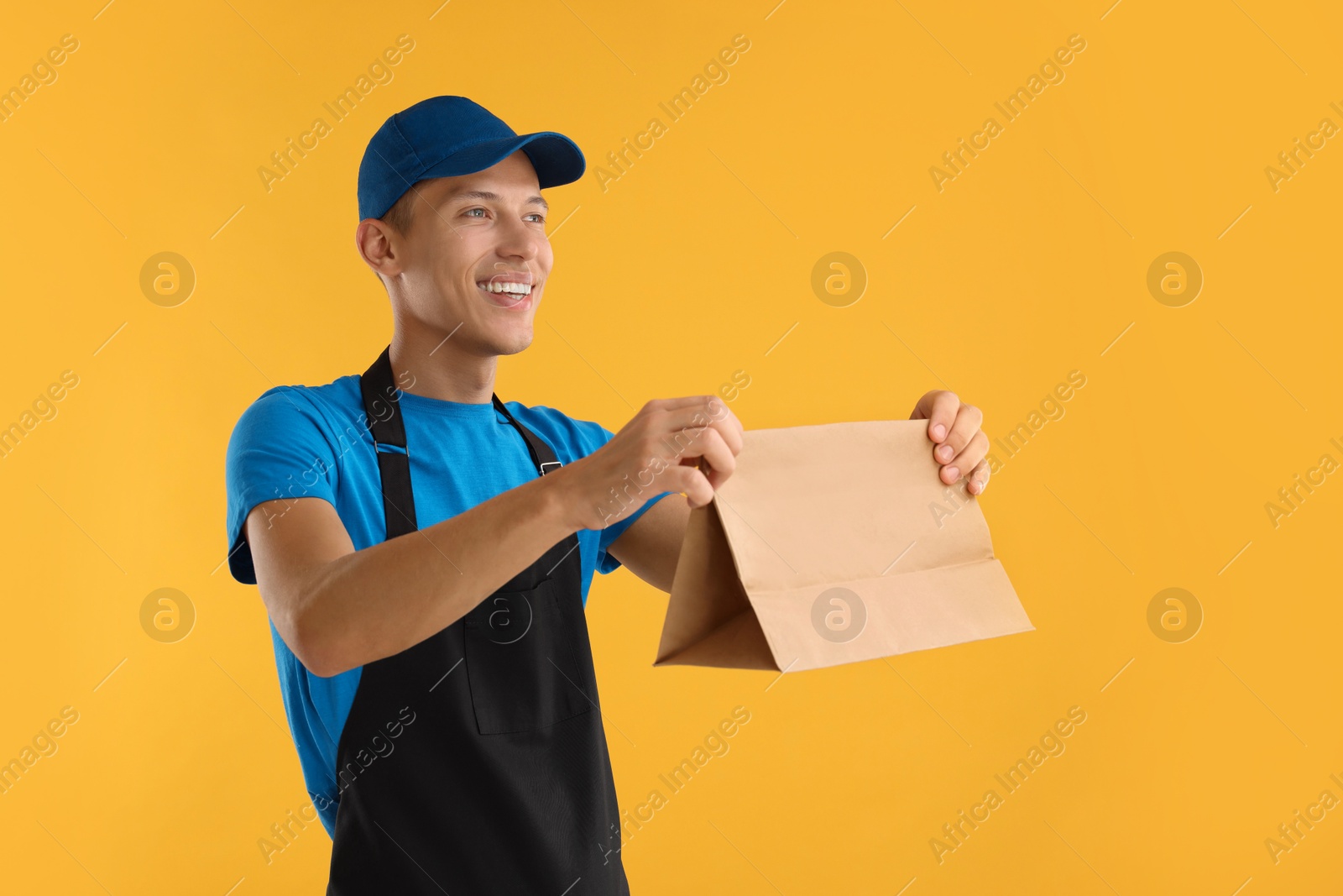 Photo of Fast-food worker with paper bag on orange background