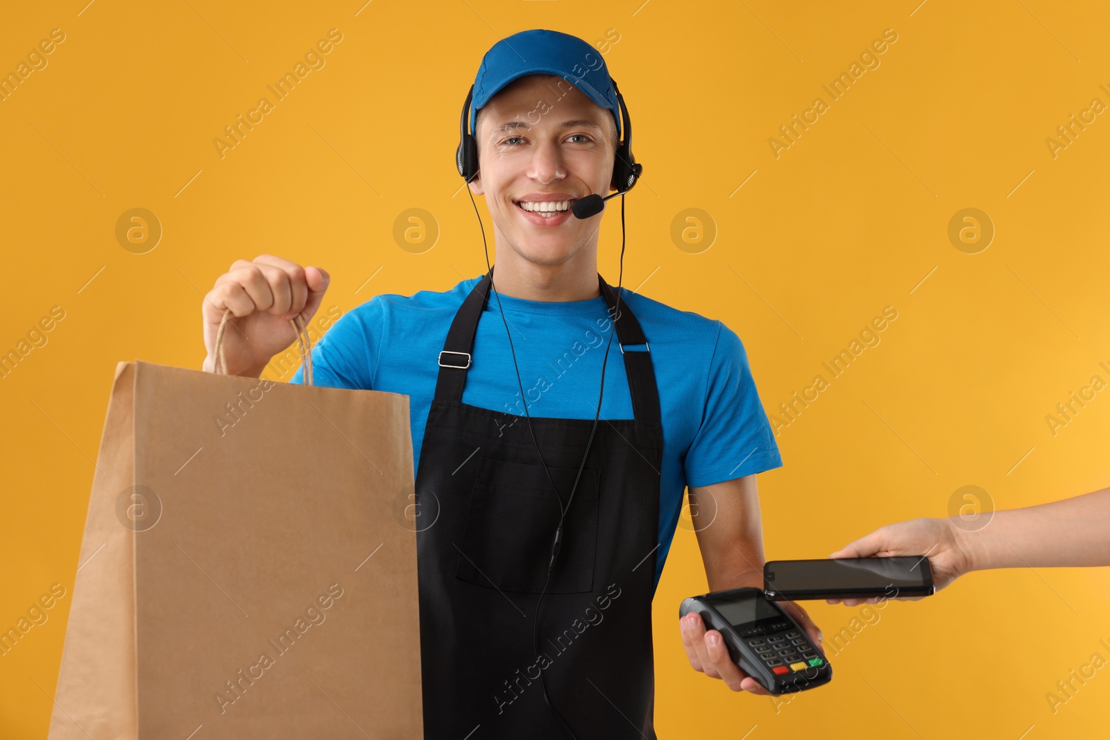 Photo of Fast-food worker taking payment from client via terminal on orange background, closeup