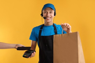 Photo of Fast-food worker taking payment from client via terminal on orange background, closeup