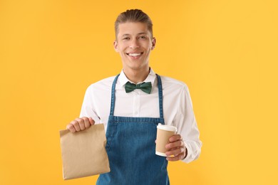 Photo of Fast-food worker with paper bag and cup on orange background