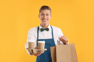 Photo of Fast-food worker with paper bags and cups on orange background