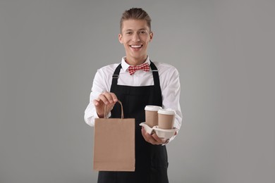 Fast-food worker with paper bag and cups on gray background