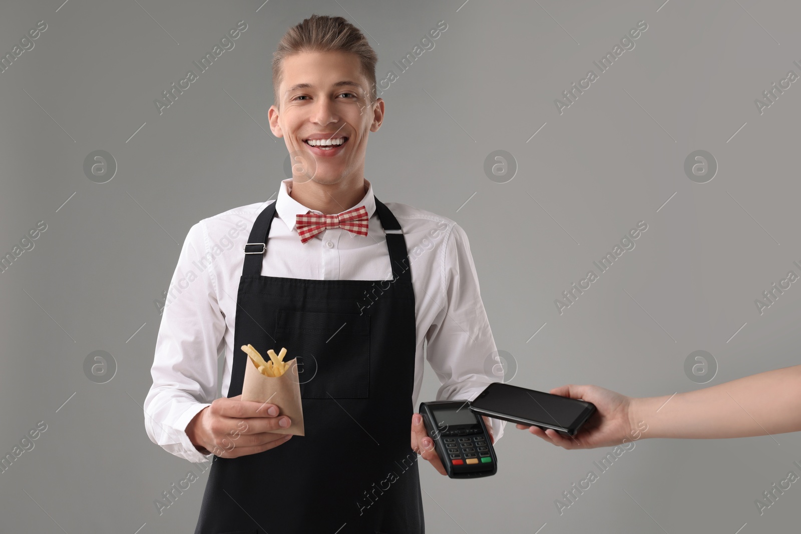 Photo of Fast-food worker taking payment from client via terminal on gray background, closeup