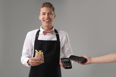 Photo of Fast-food worker taking payment from client via terminal on gray background, closeup