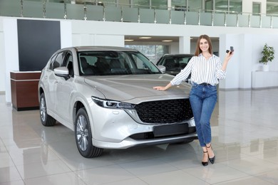 Photo of Happy young woman with key near new silver car in salon