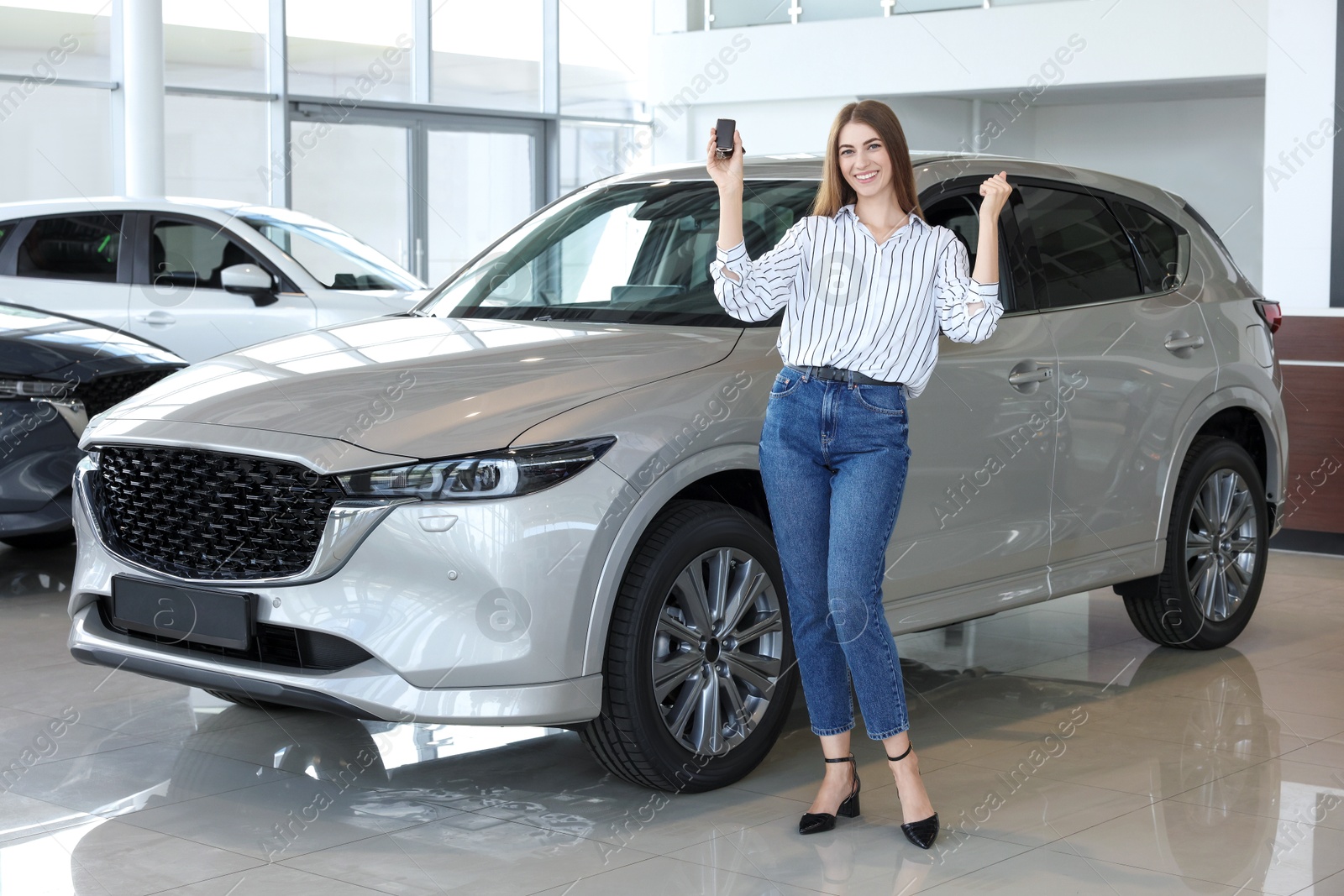 Photo of Happy young woman with key near new silver car in salon