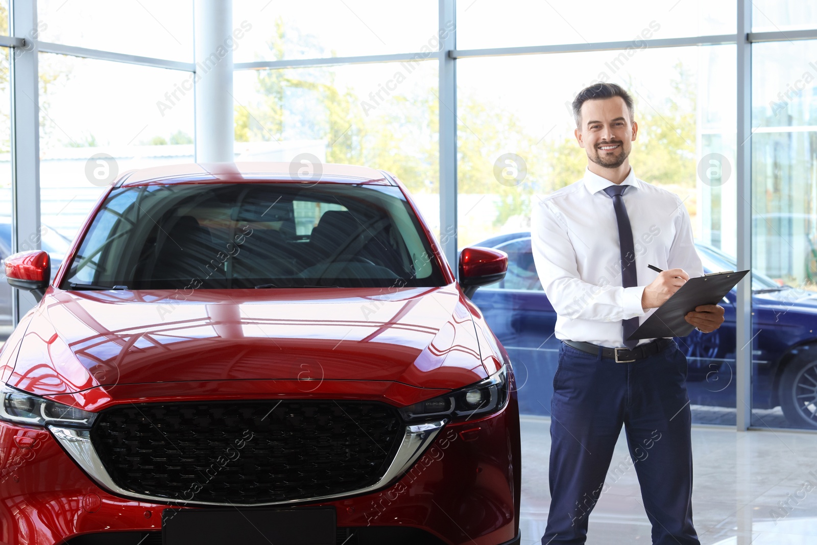 Photo of Happy salesman near new red car in salon