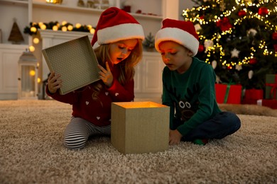 Photo of Little kids opening magic Christmas box on floor at home