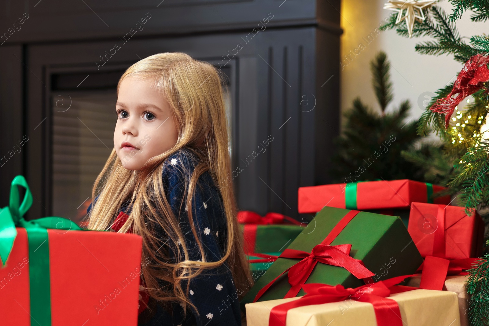 Photo of Little girl with Christmas gifts on floor at home