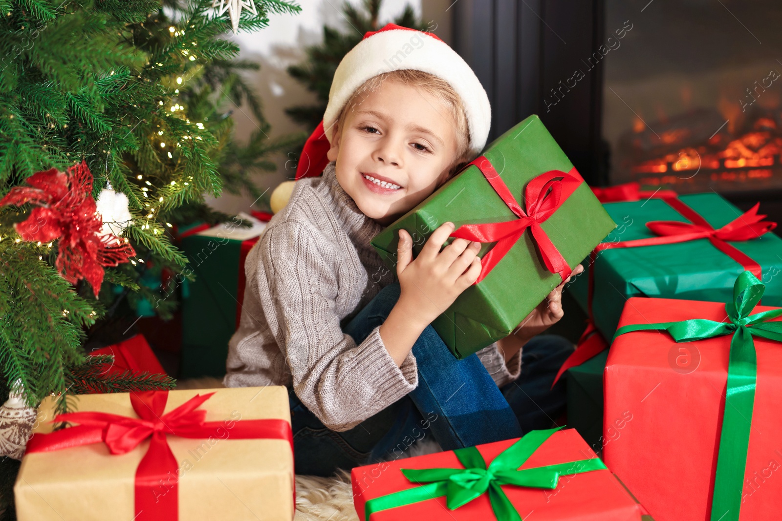 Photo of Little boy in Santa hat with Christmas gifts at home