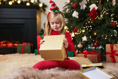 Photo of Little girl opening Christmas gift on floor at home