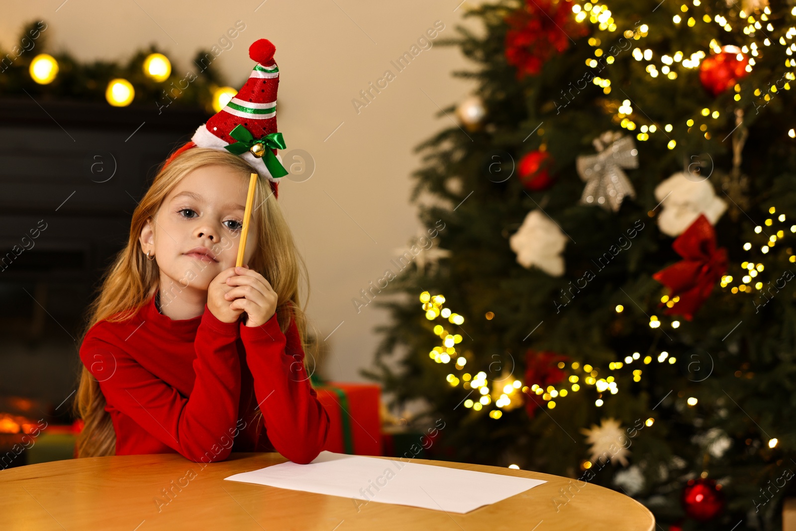 Photo of Little girl writing letter to Santa Claus at table indoors. Christmas celebration