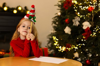 Photo of Little girl writing letter to Santa Claus at table indoors. Christmas celebration