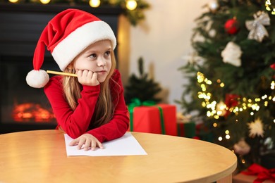 Photo of Little girl writing letter to Santa Claus at table indoors. Christmas celebration