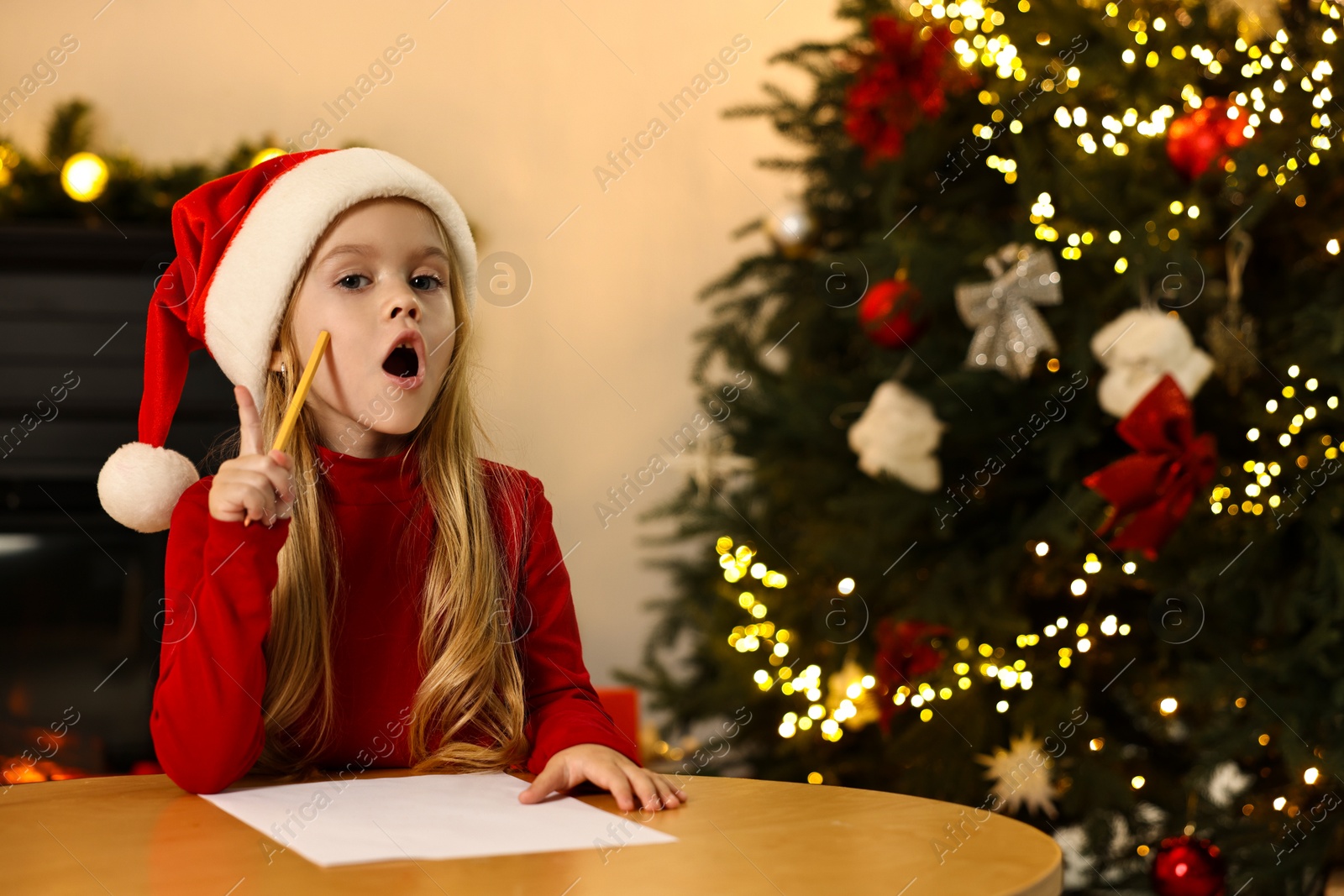 Photo of Little girl writing letter to Santa Claus at table indoors. Christmas celebration