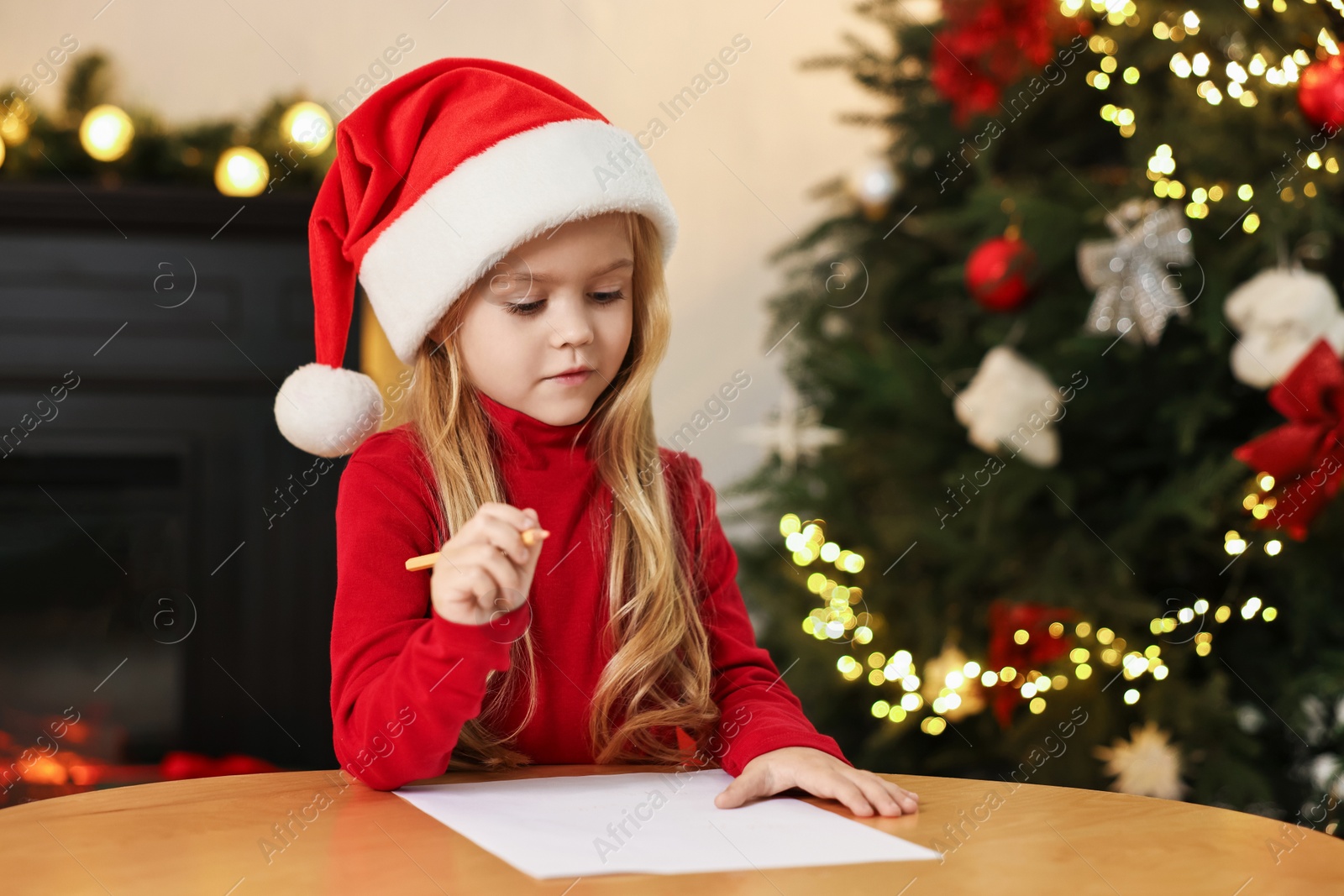 Photo of Little girl writing letter to Santa Claus at table indoors. Christmas celebration