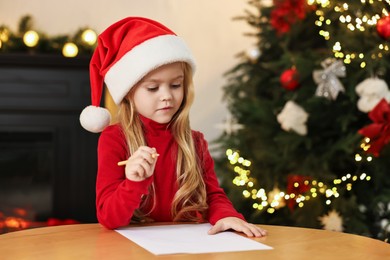 Little girl writing letter to Santa Claus at table indoors. Christmas celebration