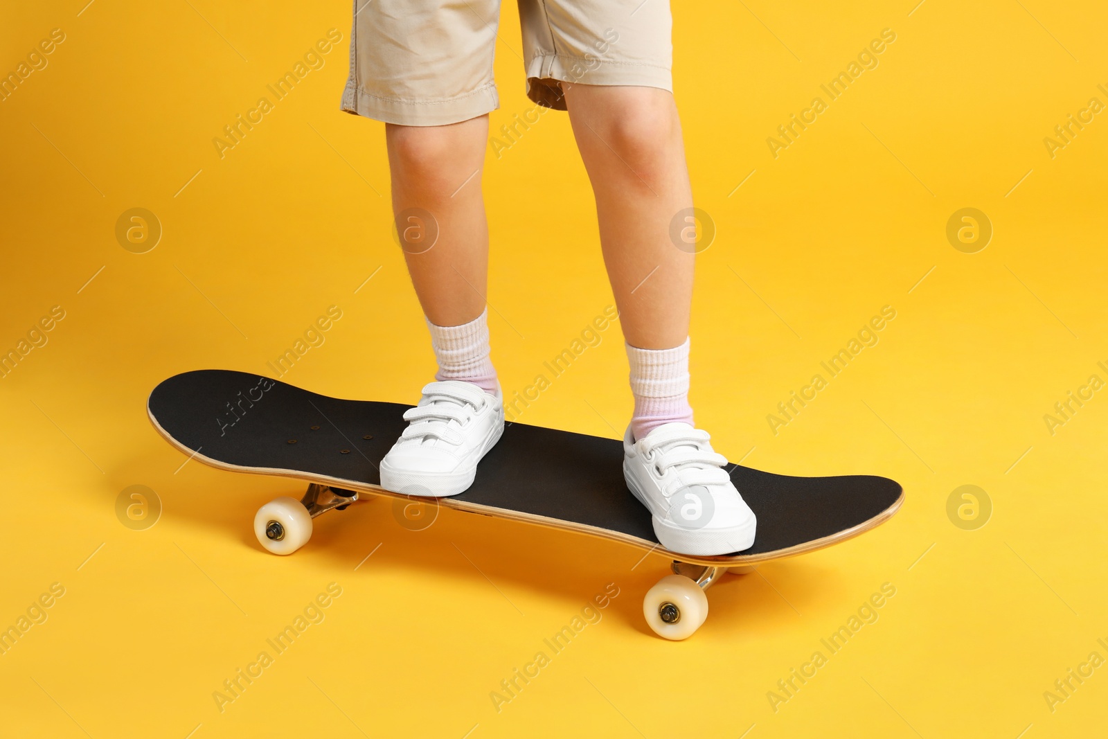 Photo of Little girl standing on skateboard against yellow background, closeup